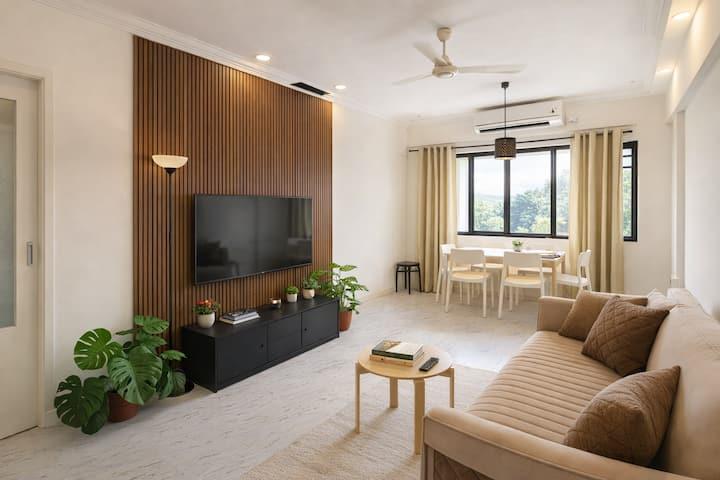 Modern 2BHK living room with a compact sofa, elegant TV wall, warm lighting and neutral finishes